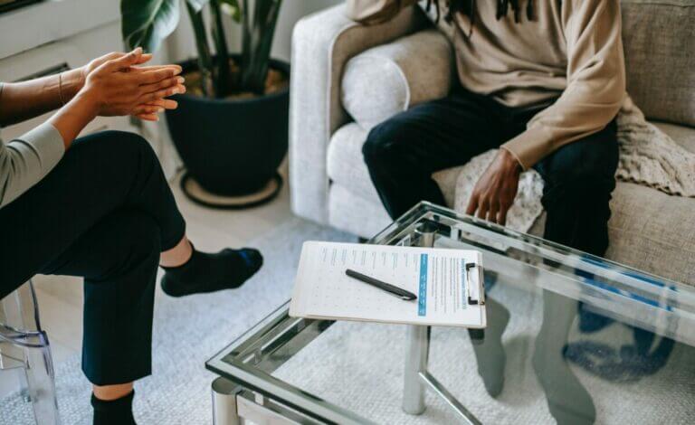 two people facing each other across a table, a clipboard on the table, coaching or counseling session